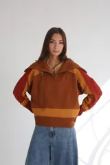 Sweater de punto color marrón con rayas horizontales color mostaza en el ruedo y en la parte superior del pecho. Tiene cuello polo con cierre de cremallera y mangas largas con detalles en color ladrillo y mostaza.