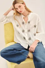 Camisa blanca de voilé de algodón con escote redondo y bordados de ojos en el delantero. De corte recto y mangas largas con puños abotonados.