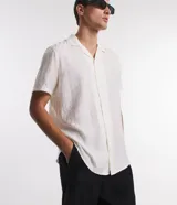Camisa boxy de hombre confeccionada en viscolino color crudo con rayas texturizadas, cuello inglés, solapa, mangas cortas y abotonado frontal.
