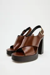 Sandalias de cuero color marrón con plataforma y tacón cuadrado. Tiras cruzadas en la parte delantera y cierre mediante tira trasera con hebilla lateral.