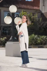 Saco largo color crudo, con cuello redondo, bolsillos frontales con apliques de cuero plateado y mangas largas.