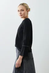 Remera negra de manga larga con cuello redondo y tachas plateadas en el cuello y los puños.