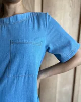 Vestido midi negro con cuello redondo y mangas cortas. Presenta dos bolsillos cuadrados en el pecho y ribetes blancos en cuello, mangas, bolsillos y ruedo.