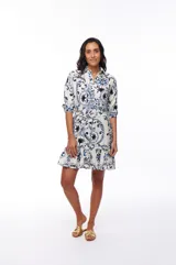 Vestido corto con estampado floral en tonos azules y negros sobre fondo blanco, corte camisero con cuello clásico, mangas 3/4 y falda con volantes.