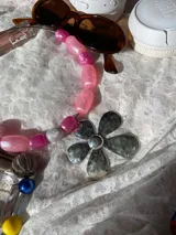 Collar con dije metálico de flor y mostacillas rosadas variadas.