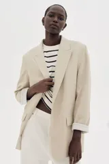Blazer color beige de corte recto, con solapas de pico, bolsillos delanteros con solapa y mangas con forro a rayas.