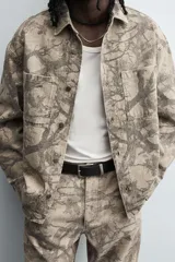 Sobrecamisa color beige con estampado abstracto en tonos grises, de corte relaxed fit, cuello solapa, manga larga con puños abotonados, bolsillos de plastrón en el pecho, efecto lavado y cierre frontal con botones.