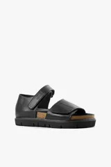 Sandalia plana negra de cuero, con tiras anchas cruzadas y ajuste con velcro.