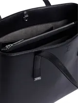 Cartera tote Calvin Klein negra de poliuretano con textura granulada. Tiene doble asa superior, cierre de cremallera y logo grabado en el frente.