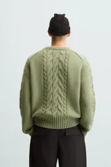 Sweater verde claro de punto con cuello redondo y mangas largas. Presenta diseño de trenzas en el centro y en las mangas.