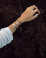 Pulsera tipo esclava abierta, con acabado rústico y textura irregular, en tono plateado. Se vende por unidad.