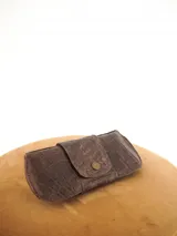 Estuche para lentes color borgoña con textura símil cocodrilo y cierre con broche a presión.