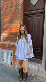 Camisa blanca de broderie con escote en V, abotonada y manga 3/4. Corte oversize, más larga atrás que adelante.