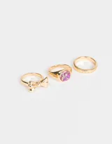 Set de tres anillos dorados: uno con un moño, otro con flores encapsuladas en resina y otro con textura acanalada.