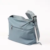 Bolso bandolera de cuero sintético color celeste, con textura granulada y correa ancha con ojales metálicos.