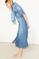 Vestido midi de denim celeste, con cuello camisero, manga corta y botonadura frontal. Presenta bolsillos superiores con solapa y botón, canesú delantero y trasero, falda acampanada y costuras decorativas.