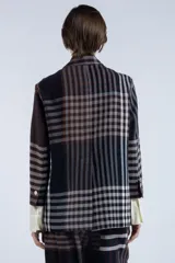 Blazer con estampado a cuadros en tonos marrones y negros, de corte recto y silueta relajada. Presenta solapas clásicas, cierre frontal con botones y bolsillos con tapa. Mangas largas con puños blancos.