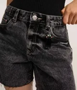 Short de jean estilo mom, color negro con efecto marmoleado (acid wash). Presenta tiro alto, trabillas para cinturón, cierre tradicional, bolsillos y ruedo cortado sin remate.