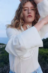 Blusa blanca de corte holgado en tejido transparente de mezcla de lyocell. Modelo de manga larga con cuello elevado de encaje, puños anchos abotonados y bajo recto. Pechera con abertura, alforzas y tiras spaghetti.