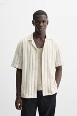 Camisa de manga corta con cuello bowling y corte relaxed fit, confeccionada en tejido con algodón y diseño a rayas verticales en tonos beige y blanco.