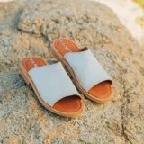 Sandalias bajas color gris claro, con capellada ancha de cuero y suela marrón.