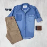 Camisa de jean celeste con cuello mao, manga larga con puños enrollados, cierre con botones y dos bolsillos frontales, uno de parche y otro con solapa y botón.