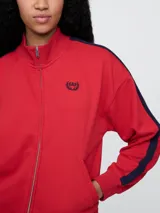 Campera deportiva Gap azul marino con cierre frontal, cuello alto y logo bordado en el pecho. Presenta dos líneas blancas verticales a lo largo de las mangas.