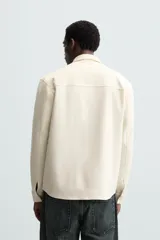 Sobrecamisa negra de tejido con elasticidad, cuello solapa, manga larga con puño abotonado, bolsillos de plastrón en el pecho y cierre frontal con botones a presión.
