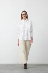 Camisa blanca de algodón con diseño utilitario y calce relajado. Presenta dos bolsillos frontales de estilo cargo con tapa y costuras a contratono.