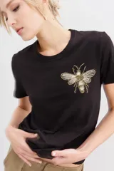 Remera negra de algodón con calce al cuerpo, mangas cortas y cuello redondo. Presenta un bordado frontal de abeja con canutillos dorados y plateados.