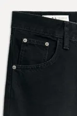 Pantalón de jean negro de corte amplio, tiro alto, con trabillas y cinco bolsillos. Cierre frontal con cremallera y botón metálico.