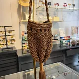 Bolso limosnero marrón tejido en macramé, con flecos largos y asa trenzada.