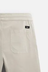 Bermuda color verde militar de corte relajado, confeccionada en tejido de algodón. Tiene cintura elástica ajustable con cordón interior, bolsillos frontales y bolsillo trasero de parche.