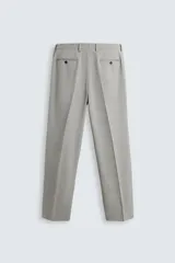 Pantalón de vestir gris claro, de corte recto, confeccionado en tejido con lana. Cuenta con bolsillos frontales y traseros de doble vivo con botón. Cierre frontal con cremallera y botón.
