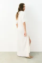 Vestido tobillero de punto de algodón suave color blanco, de corte holgado con cuello redondo, mangas dolman hasta el codo y tajo largo delantero con argolla metálica y cuenta decorativa para efecto drapeado.