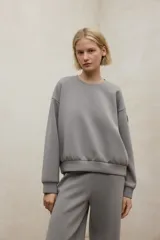 Buzo de tejido liso color gris, con cuello redondo y puños y ruedo ajustados.