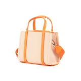 Cartera mini tipo tote bag bicolor, con cuerpo de tela color beige y solapa frontal de cuero sintético color naranja. Tiene doble asa de mano, correa larga regulable y herrajes plateados. Presenta un bolsillo externo con cierre y dos bolsillos internos, uno con cierre y otro abierto.