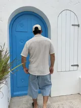 Camisa tejida a rayas verticales color beige y blanco, de corte recto, manga corta y cuello cubano.