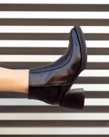 Botín corto de cuero negro, estilo cowboy moderno, con textura de cocodrilo en la caña y puntera cuadrada. Posee un tacón ancho y geométrico, y cierre lateral.