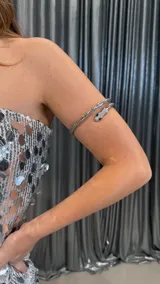 Brazalete rígido plateado con forma de serpiente enroscada, con cabeza decorada con strass y ojos negros.