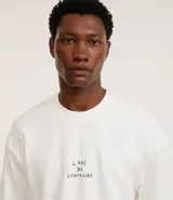 Remera boxy de algodón color crudo, con cuello redondo y mangas cortas. Estampa frontal con la frase "l'ami du contraire" y estampa trasera de figuras estilo art noveau.