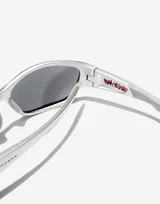 Lentes de sol unisex plateados, con montura rectangular envolvente y lentes espejadas celestes. Patillas con logo de Hawkers y detalle de texto en rojo.