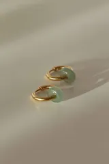 Par de aros tipo argolla dorados con dije de piedra natural con patrón de manchas negras sobre fondo blanco.