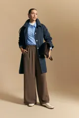 Trench color beige de corte clásico con cuello amplio, botones frontales, detalles en los hombros y mangas largas.