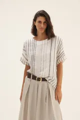 Blusa blanca con rayas verticales grises, corte holgado, mangas cortas con detalle desflecado y cuello redondo.