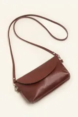 Cartera tipo sobre de cuero vacuno, con solapa frontal, cierre y broche magnético. Incluye correa larga ajustable y extraíble para usar como bandolera.