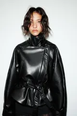 Cazadora negra de efecto piel, con cuello solapa y manga larga acabada en puño. Tiene bolsillos de vivo en delantero, cinturón lazada en mismo material y bajo acabado peplum. El cierre frontal es con cremallera.