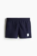 Short de baño azul marino de nylon con elástico revestido y cordón para ajustar oculto en la cintura, bolsillos laterales y bolsillo de solapa con cierre autoadherente atrás. Largo por encima de la rodilla con abertura corta en los laterales y suspensor interior en malla suave.