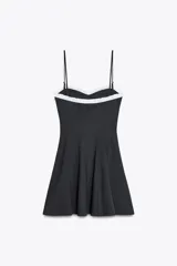 Vestido corto negro con tirantes finos ajustables, escote recto con volantes blancos y lazo decorativo. Cierre lateral con cremallera oculta.