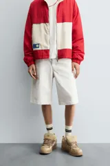 Bermuda de denim color blanco roto con efecto encerado, corte amplio (baggy fit) y cinco bolsillos. Presenta cierre frontal con cremallera y botón.